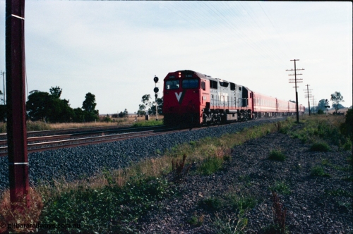145-23
Wallan, Boundary Rd crossing, V/Line broad gauge N class N 466 'City of Warrnambool' Clyde Engineering EMD model JT22HC-2 serial 86-1195 leads a 5 car Z set on a down pass, the standard gauge tracks and up home signal for Wallan Loop are on the left.
Keywords: N-class;N466;Clyde-Engineering-Somerton-Victoria;EMD;JT22HC-2;86-1195;