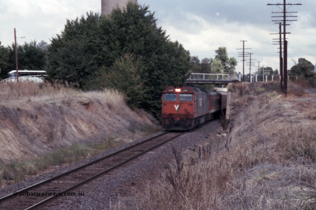 148-30
Wangaratta, V/Line standard gauge G class G 520 Clyde Engineering EMD model JT26C-2SS serial 85-1233 leads the down Inter-Capital Daylight under the station access bridge with town water tower behind bushes, broad gauge yard and station is to the right of image.
