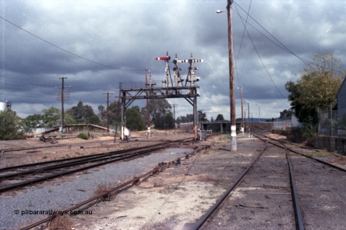 148-26
Wangaratta, Signal Bridge at Down end of yard, looking south, Up Signal Post 9 was one arm and two discs, the Arm Home Signal from 'A' to No. 1 Road to Post 20, the removed discs were from 'A' to Siding 'F' and from 'A' to Cattle Sidings. Down semaphore and disc Signal Posts 7, 8 and 10 facing away, rodding for mainline points visible, fuel siding at left with footbridge over standard gauge line, Roy Street overbridge in the distance, Sidings E and Works platform at right.
