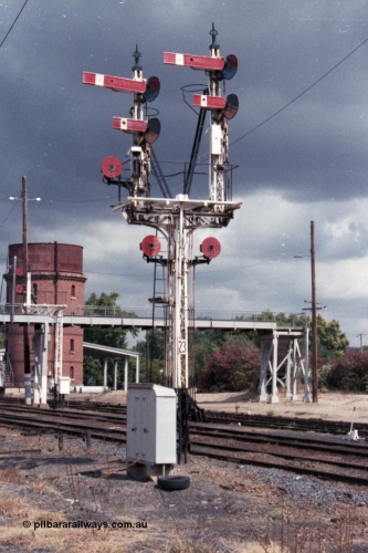 148-29
Wangaratta, Bracket Post 23, four arms and three Discs Up Signals, Top arm on Left-hand Doll Home Signal from Main Line to No.1 Road to Post 12. Bottom arm on Left-hand Doll Calling-on signal from Main Line to No. 1 Road towards Post 12. Disc on Left-hand Doll from Main Line to Siding 'A'. Top arm on Right-hand Doll Home Signal from Main Line to No. 2 Road to Post 14. Bottom arm on Right-hand Doll Calling-on Signal from Main Line to No.2 Road towards Post 14. Left-hand Disc on Post from Main Line to No. 2 Road towards Post 15. Right-hand Disc on Post from Main Line to No. 4 or 5 Roads towards Post 16. Footbridge, water tower and Disc Signal Post 21 in the background.
