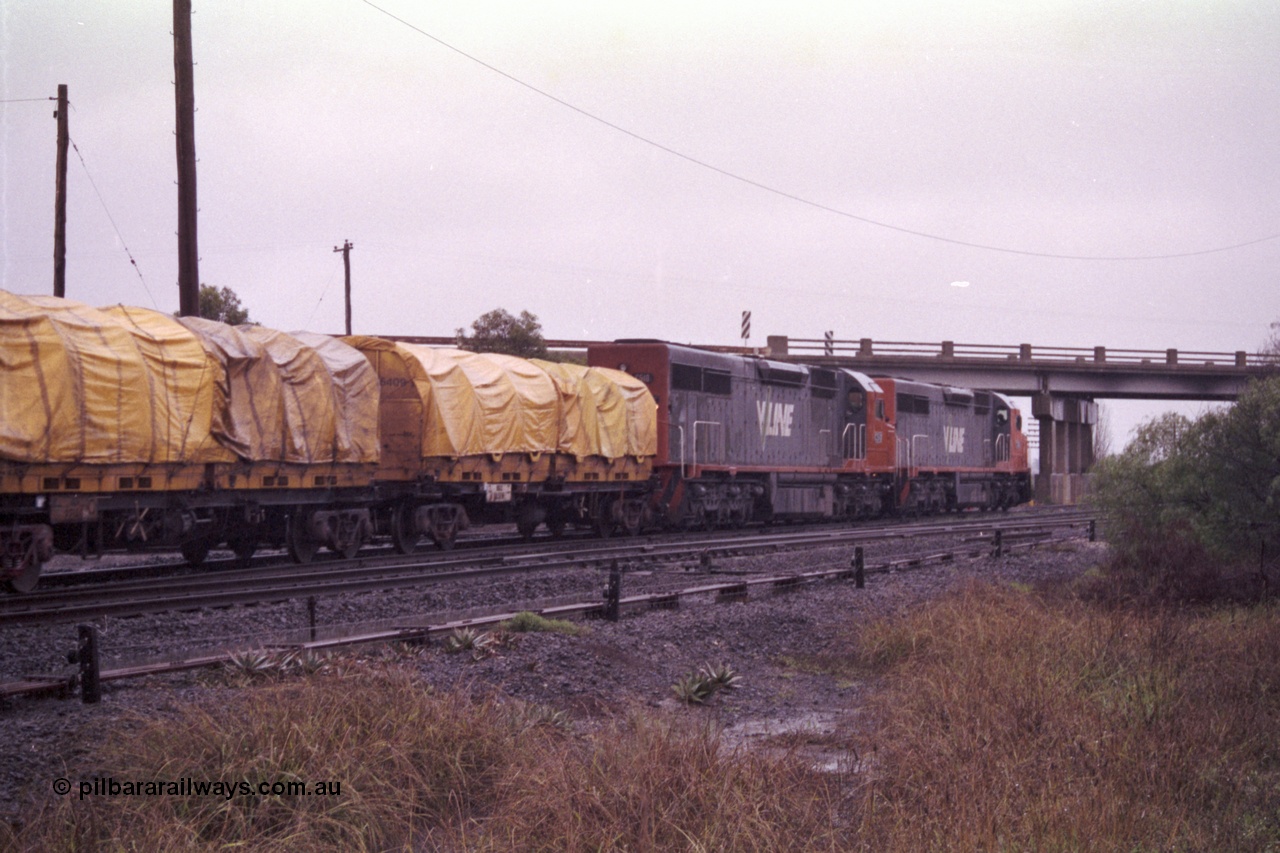 150-12
Gheringhap, broad gauge V/Line C class locos C 506 Clyde Engineering EMD model GT26C serial 76-829 and C 510 serial 76-833 lead down Adelaide goods train 9169 along the Maroona line, Ballarat line, point rodding and signal wires in foreground, trailing view.
