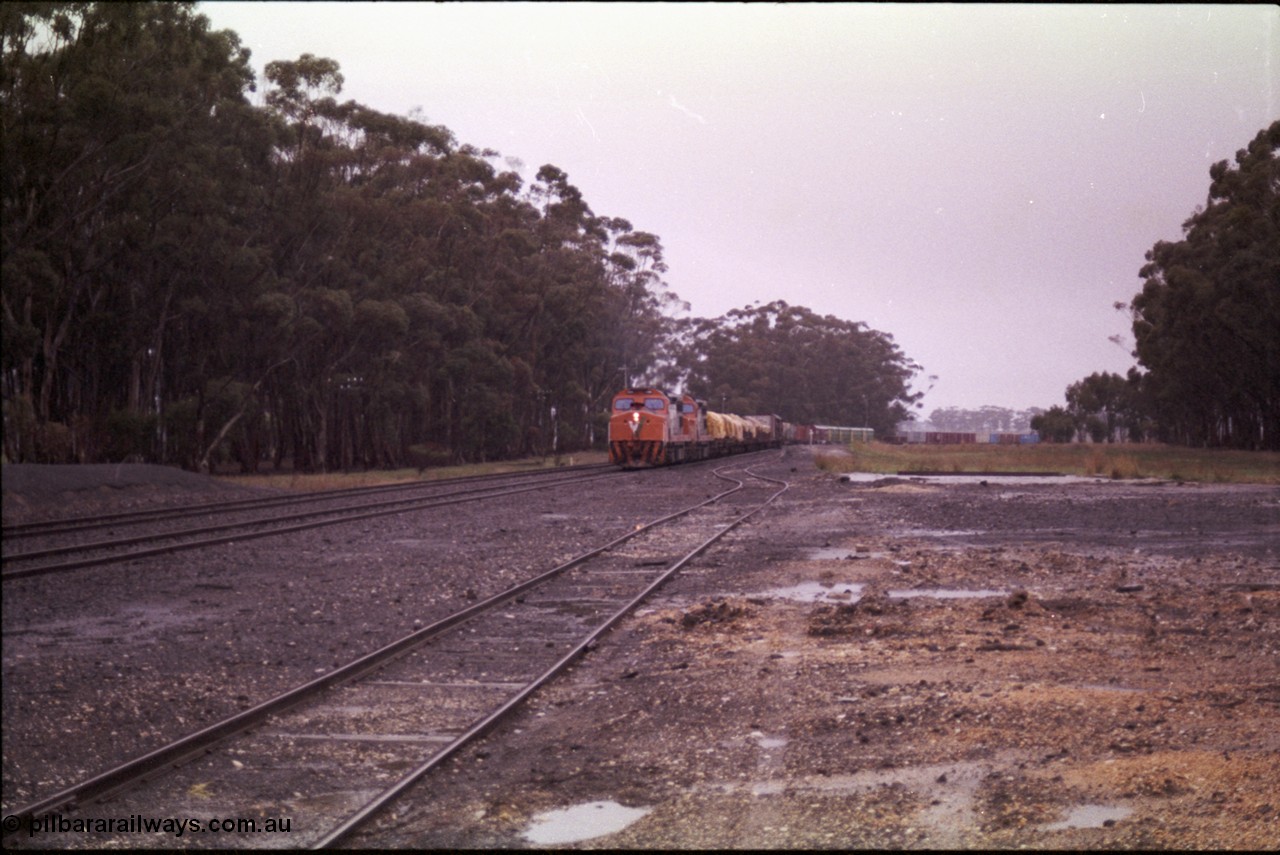 150-15
Lismore, station yard overview looking towards Melbourne from goods loading ramp, V/Line broad gauge C classes C 506 Clyde Engineering EMD model GT26C serial 76-829 and C 510 serial 76-833 leading Adelaide bound goods train 9169 through the trailable points onto No. 2 road, the goods loop or No. 3 road is closest to camera.
