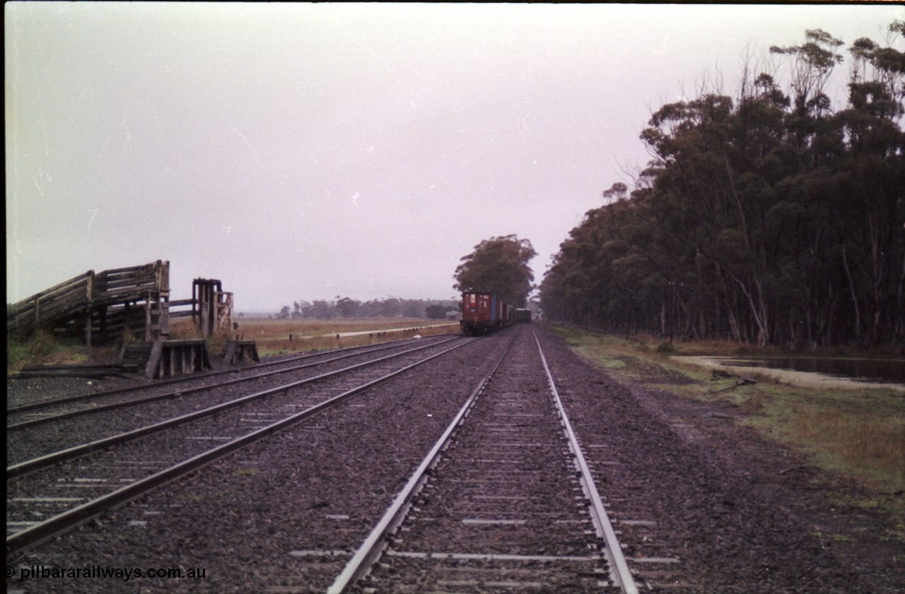 150-18
Lismore, station yard and stock loading race, sheep race closest to camera with cattle race behind, looking towards Maroona from No. 1 road, V/Line broad gauge Adelaide bound goods train 9169 exiting No. 2 and re-joining the mainline through the trailable points.
