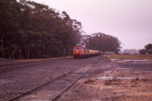 150-15
Lismore, station yard overview looking towards Melbourne from goods loading ramp, V/Line broad gauge C classes C 506 Clyde Engineering EMD model GT26C serial 76-829 and C 510 serial 76-833 leading Adelaide bound goods train 9169 through the trailable points onto No. 2 road, the goods loop or No. 3 road is closest to camera.
