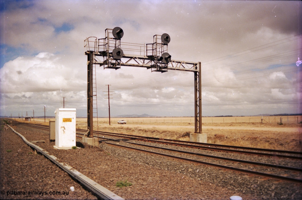 153-1-05
Bank Box Loop signal gantry at the east end, looking towards Bacchus Marsh, relay room in the background, train control phone booth next to gantry, searchlight up home signals 10 for mainline departure and 12 for loop departure.
