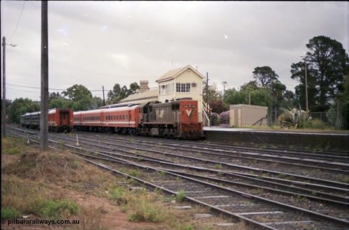 153-1-02
Bacchus Marsh, station yard overview, V/Line broad gauge loco X class X 42 Clyde Engineering EMD model G26C serial 70-705 long end leading and N set with an up passenger service for Melbourne, station platform, elevated signal box, platform shed, stabled pass consist in yard.
Keywords: X-class;X42;Clyde-Engineering-Granville-NSW;EMD;G26C;70-705;