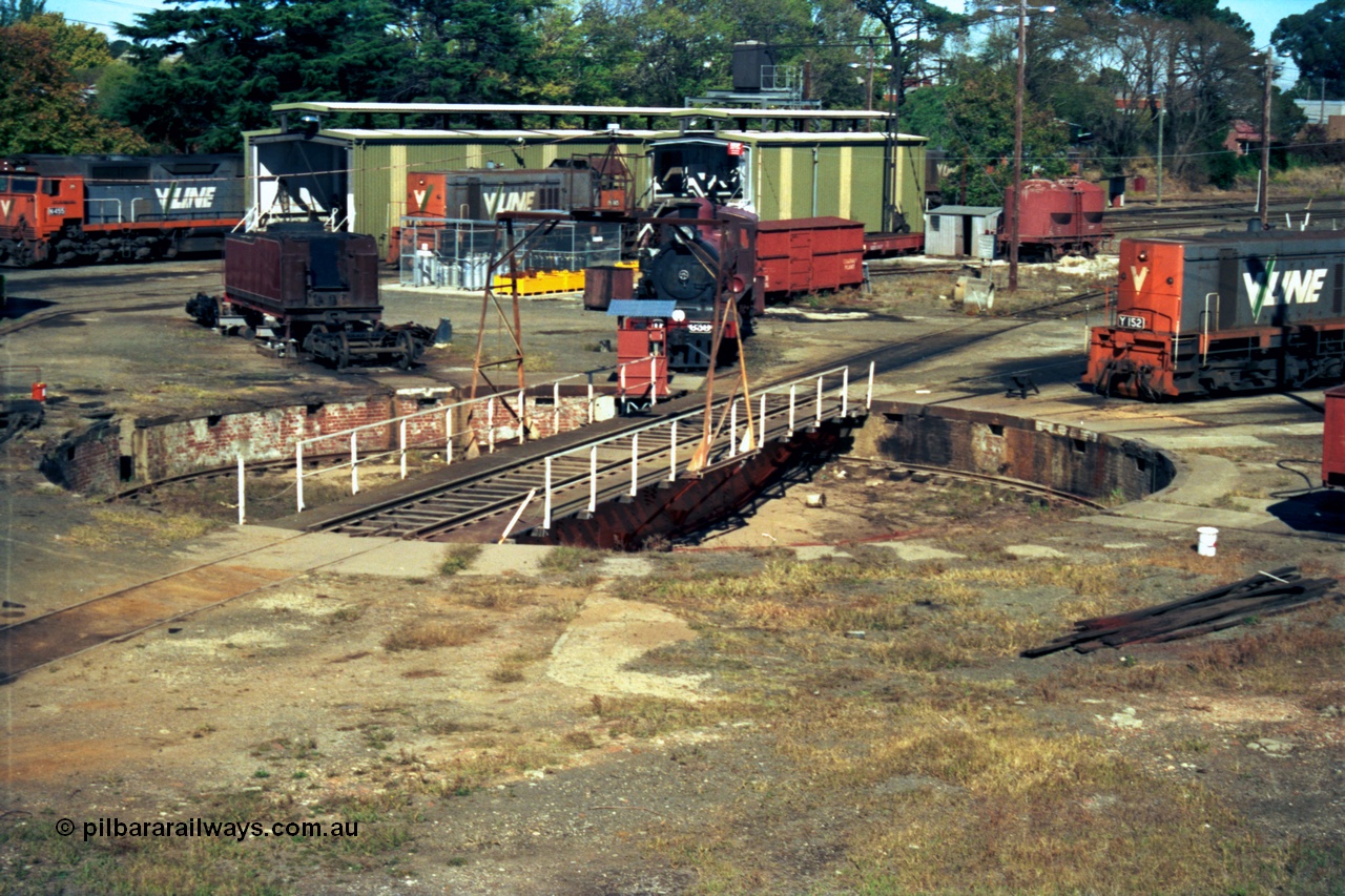153-2-08
Ballarat East loco depot turntable and pit overview, shows renumbered D3 658 as 639 being rebuilt, grounded HD type waggon behind and J type four wheel sand waggon, fuel and sanding point behind the D3, Y classes Y 152 Clyde Engineering EMD model G6B serial 67-572 and Y 165 serial 68-585, N class at left.
