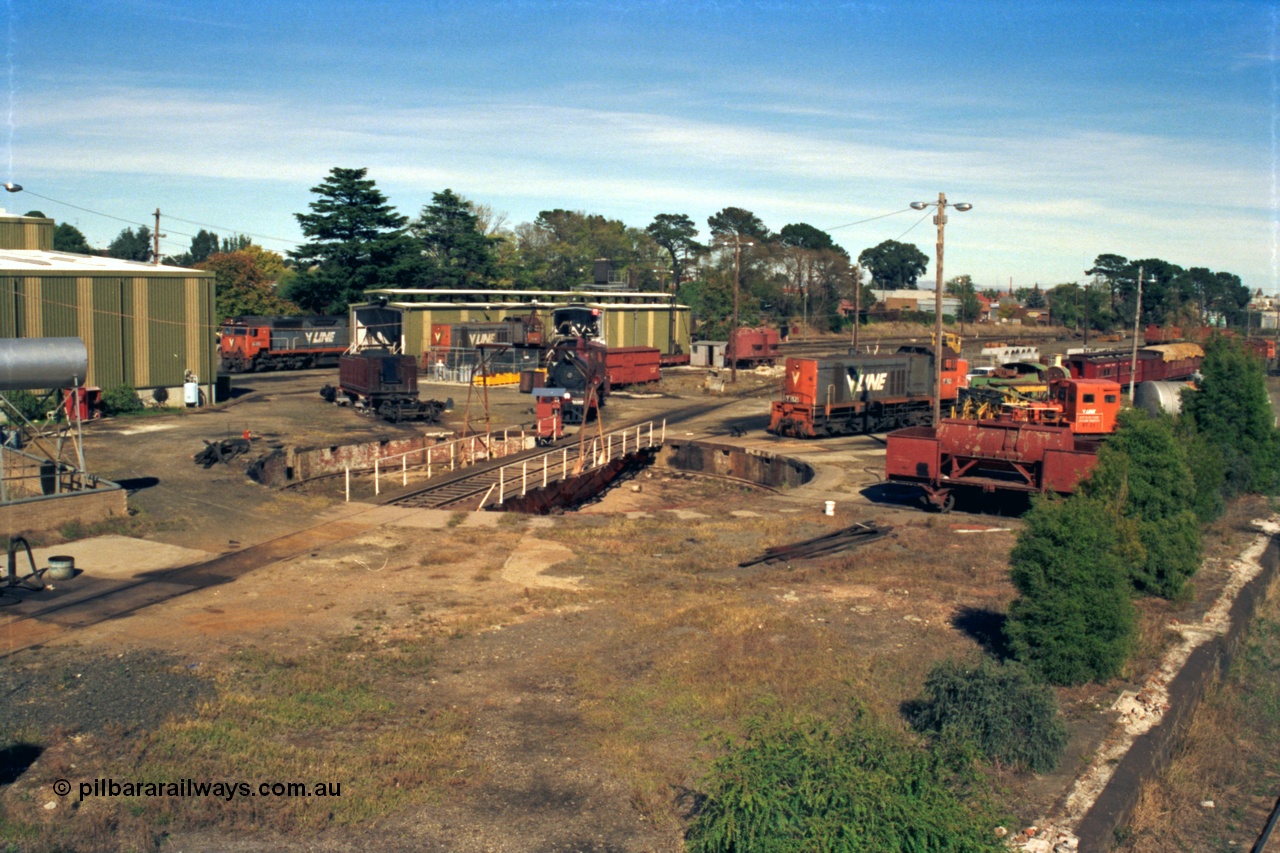 153-2-09
Ballarat East loco depot overview, broad gauge locos and waggons, turntable recently repainted and pit, D3 658 renumbered as 639 following the original being scrapped, steam engine and tender under rebuild, N class N 455 'City of Swan Hill' Clyde Engineering EMD model JT22HC-2 serial 85-1223, Y classes Y 165 Clyde Engineering EMD model G6B serial 68-585 and Y 152 serial 67-572 and RT class rail tractor RT 21? and four wheel waggons of J, HD and WT types, fuel point and sanding shed between the N class and Y class in the background.
