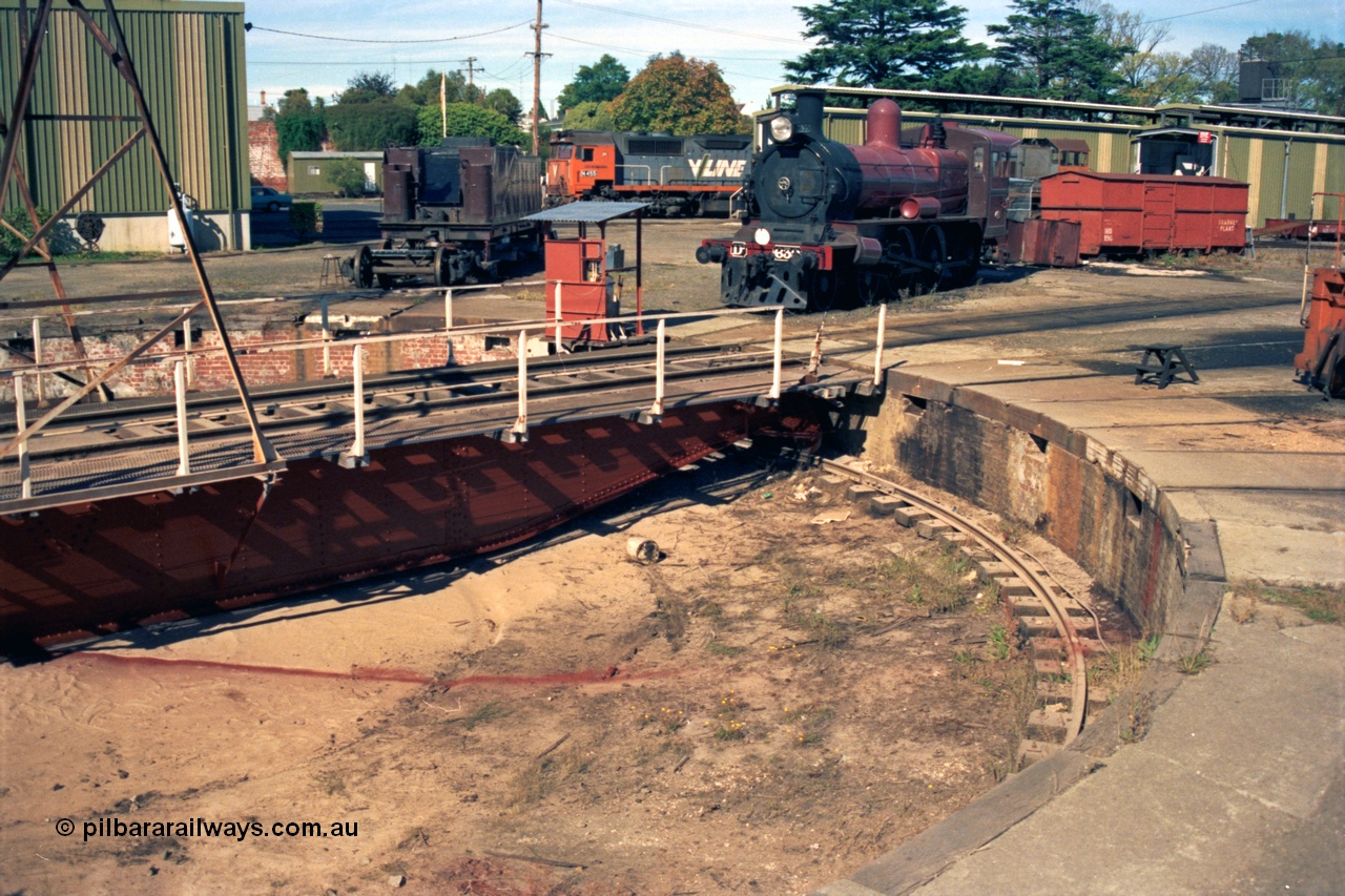153-2-10
Ballarat East loco depot turntable and pit, shows freshly painted frame, D3 639 renumbered from 658 undergoing rebuild, V/Line broad gauge N class N 455 'City of Swan Hill' Clyde Engineering EMD model JT22HC-2 serial 85-1223 obscured Y class Y 165 Clyde Engineering EMD model G6B serial 68-585, grounded four wheel HD type waggon HD 196 'Gradall Plant'.
