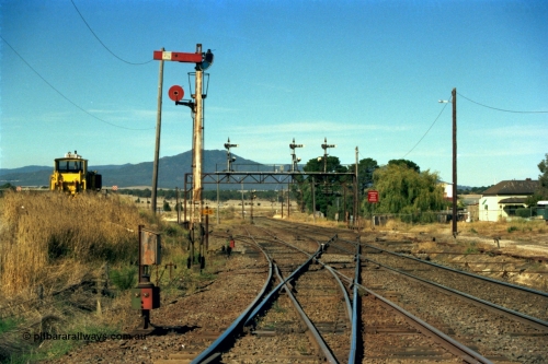 153-2-34
Ararat station yard overview looking towards Melbourne, tracks are from left, line to Maryborough, loco depot, main Western Line to Ballarat, line to Maroona, Semaphore signal and disc post 7, telephone cabinet and point indicators, signal gantry has post 4, 5 and 6, double disc post in background is post 3 from loco depot, point rodding can be seen at right crossing drain, ballast regulator at left.
