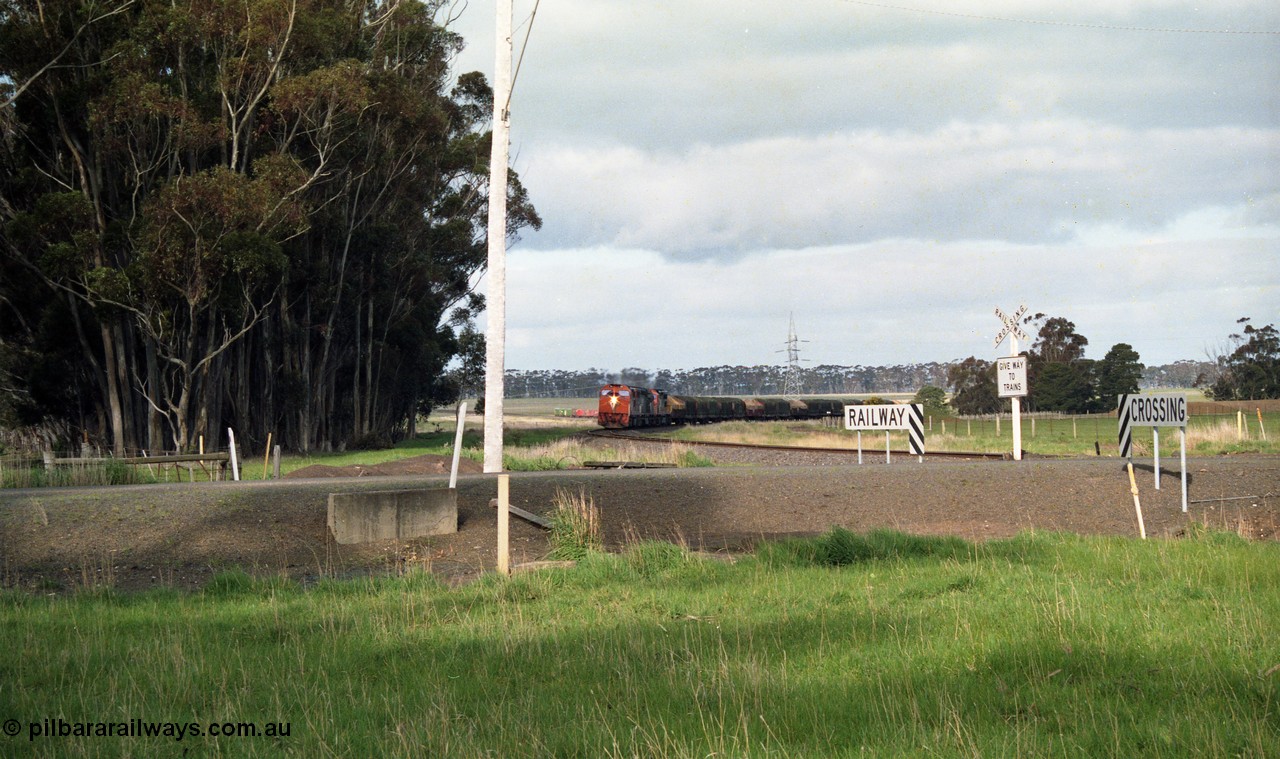 154-09
Lismore, track view looking back towards Geelong, V/Line broad gauge goods train 9169 on the curve behind triple C class locomotives Clyde Engineering EMD model GT26C, looking across Gnarpurt Road crossing.
