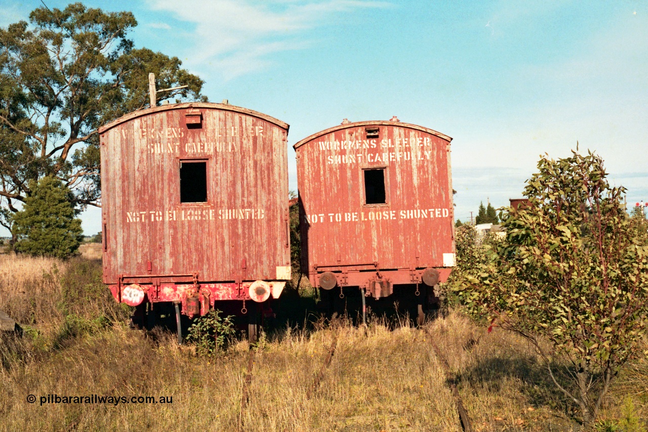 155-11
Wallan, stored 'OFF REG' waggon awaiting scrapping, bogie Ways and Works workmen's sleeper waggons, end view shows coupler, buffers and signage, the water tank can be seen behind the tree at right and the double disc signal post 15 at extreme right.
