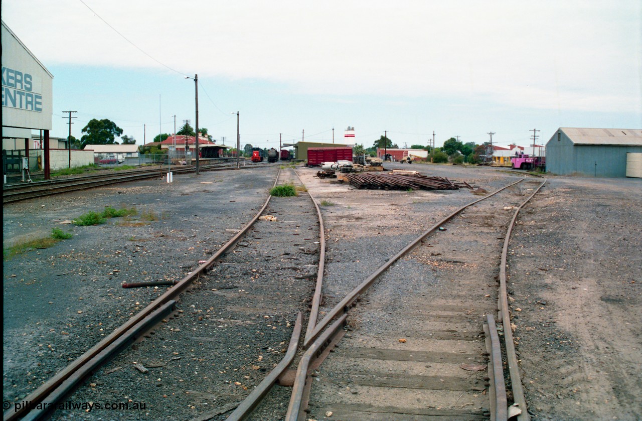 156-10
Shepparton station yard overview looking south down No.5 Road towards the goods shed and stabled T class, fuel train and louvre vans, the former Fruit Siding curves around the back of the goods shed at right, grounded B van and per way stockpiles of rails and pipes in middle of frame, station building and platform on the left, awning of Tubemakers at left over former Engine Track.
