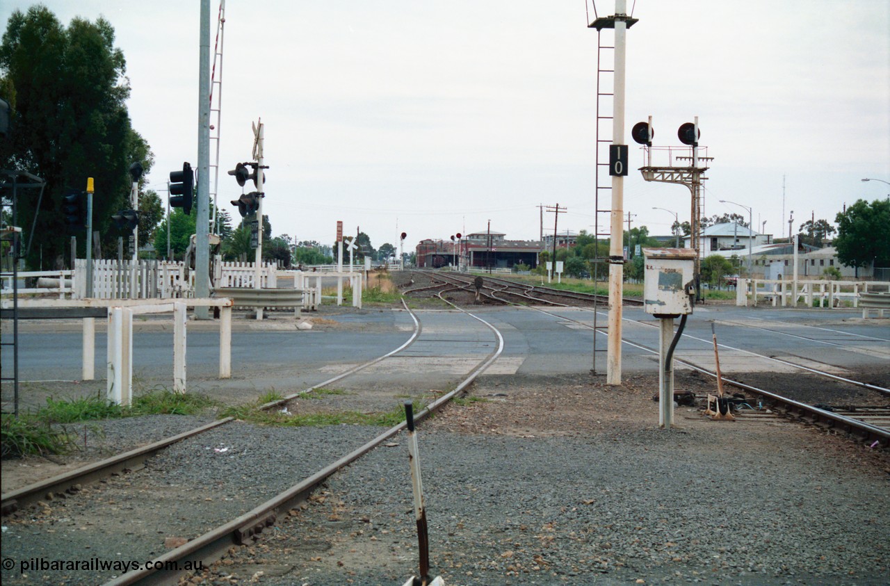 156-11
Shepparton station yard view looking north across High Street grade crossing, dwarf signal 8 just across road, SPC Siding and building in the background, searchlight signals in the distance are up and down home signals at Fryers Road grade crossing, down home signal post 10 and up home signal post 12, point lever, electric interlocking and phone cabinet.
