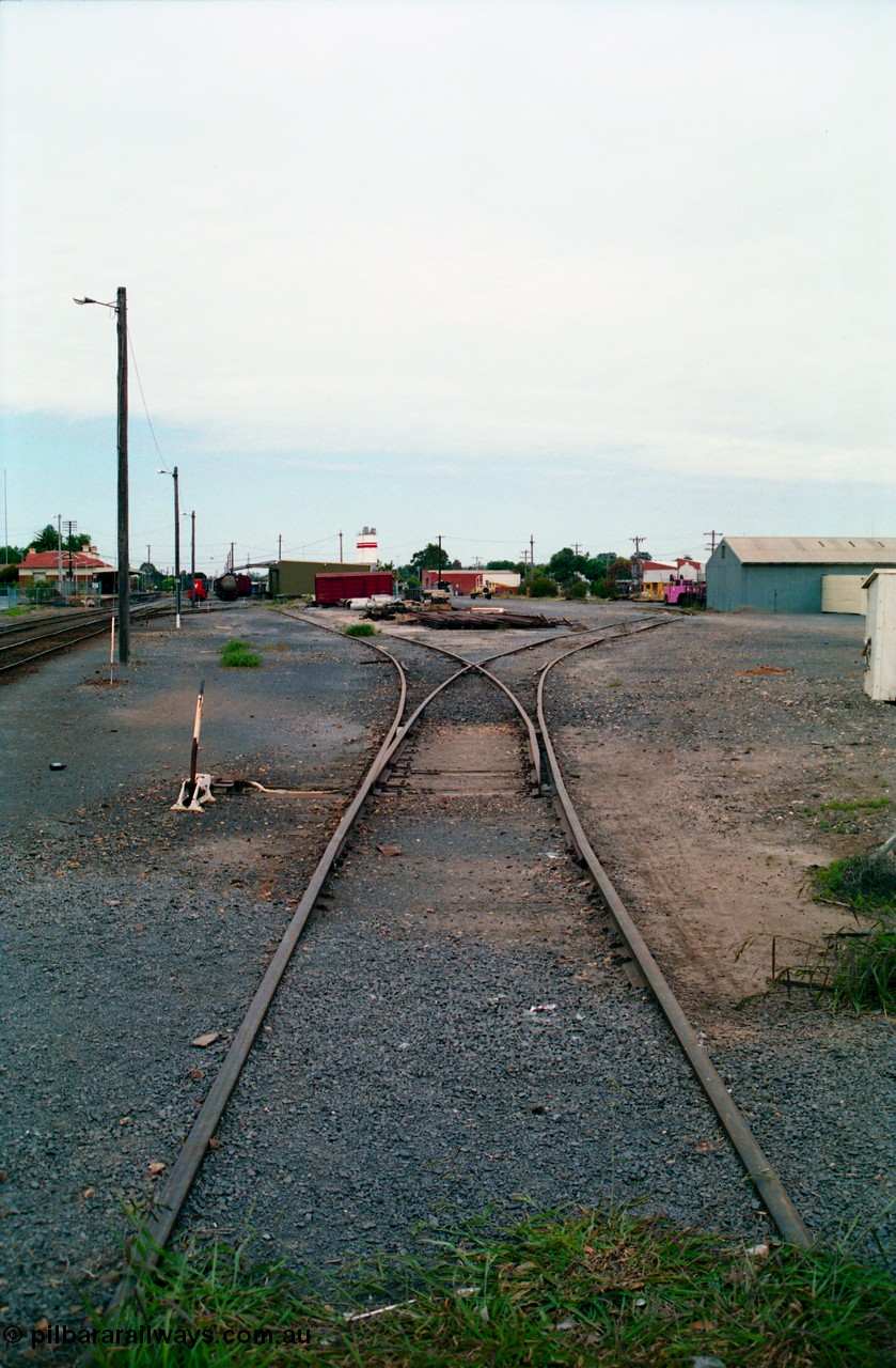 156-13
Shepparton station yard overview looking south at the No.5 Road points and lever towards the goods shed and stabled T class, fuel train and louvre vans, the former Fruit Siding curves around the back of the goods shed at right, grounded B van and per way stockpiles of rails and pipes in middle of frame, station building and platform on the left.
