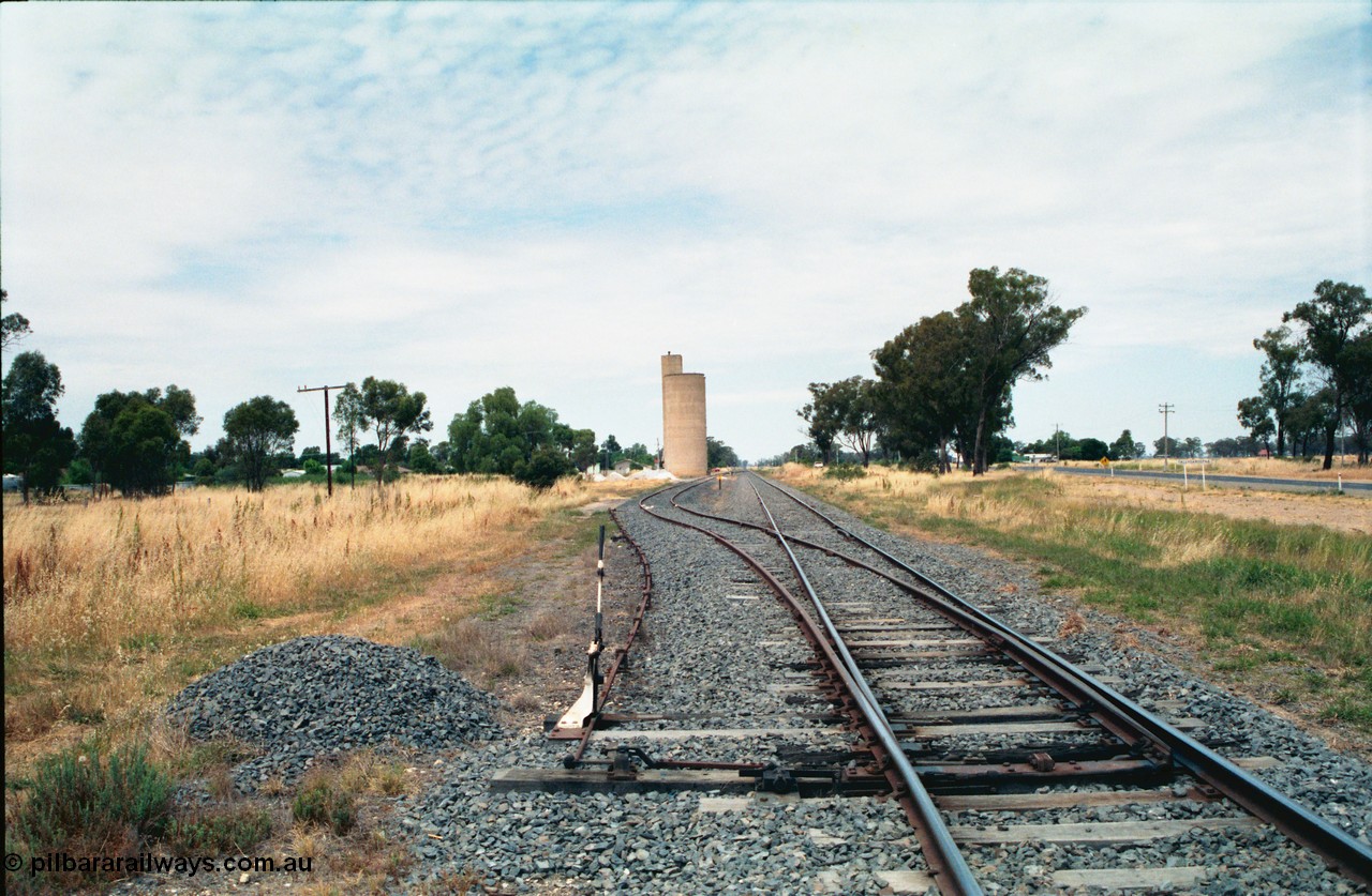 156-19
Tallygaroopna, station yard overview looking south, mainline points for siding with lever and staff lock interlocking, point rodding for derail, Williamstown style silo complex.
