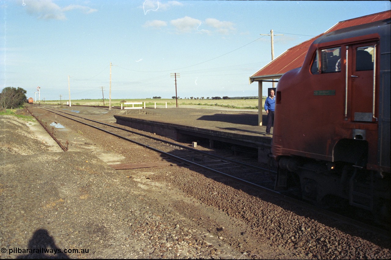 157-01
Gheringhap, station view looking east from former up platform, V/Line broad gauge A class A 77 Clyde Engineering EMD model AAT22C-2R serial 83-1181 rebuilt from B 77 Clyde Engineering EMD model ML2 serial ML2-18 leads the up Ararat to Melbourne via Nth Geelong passenger train, as the signaller prepares to swap electric staves with the crew, a down grain train 9121 sits in Siding A, station platform, point rodding and semaphore signals.
Keywords: A-class;A77;Clyde-Engineering-Rosewater-SA;EMD;AAT22C-2R;83-1181;rebuild;bulldog;