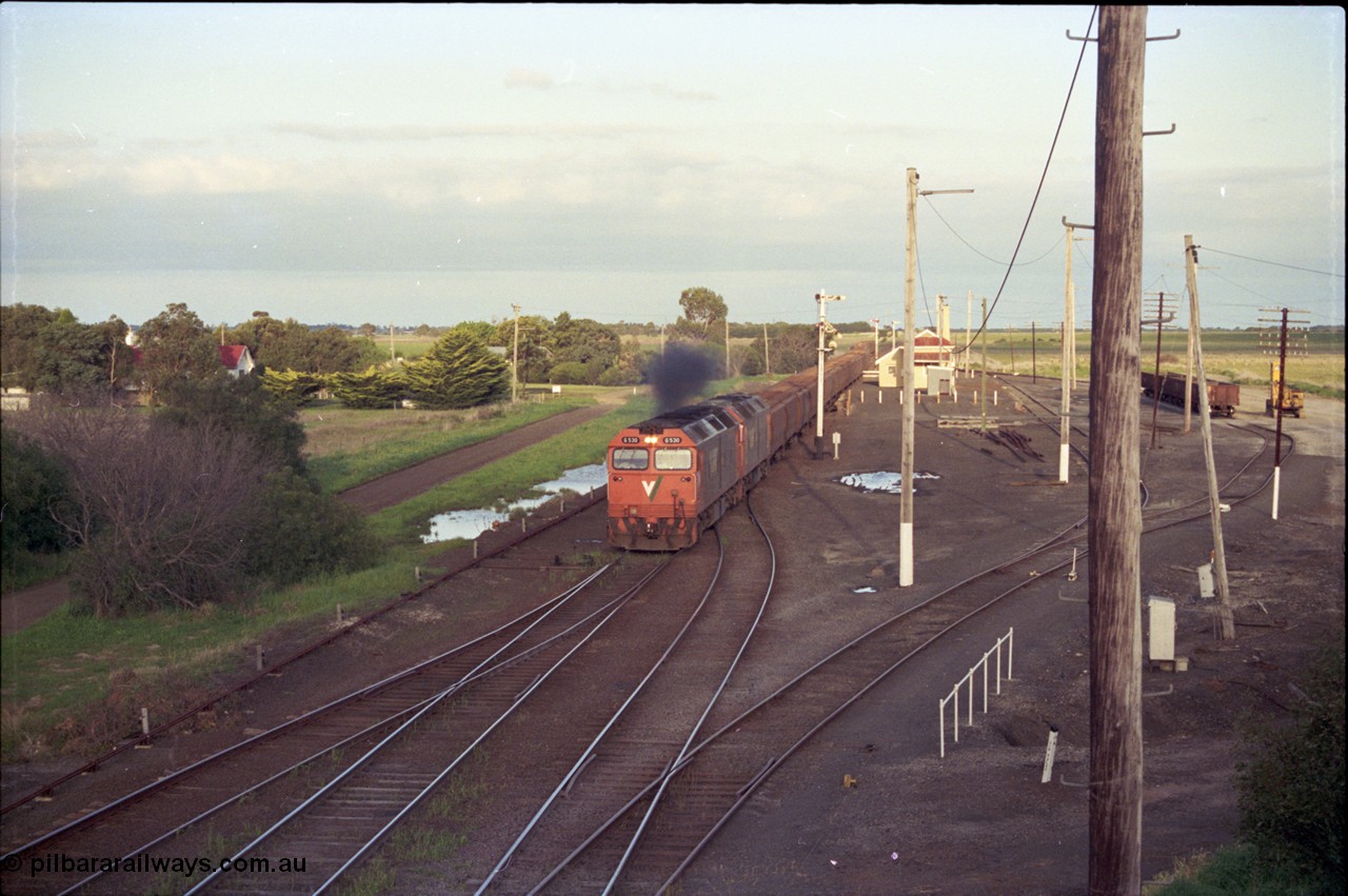 157-06
Gheringhap station yard overview from the Midland Highway overbridge, V/Line broad gauge G class G 530 Clyde Engineering EMD model JT26C-2SS serial 88-1260 leads a sister with down grain train 9123 as it powers down the straight on the Ballarat line, semaphore signal post 4 is pulled off for the Ballarat line, point rodding and signal wires on the left, the points and Siding C just visible bottom left corner, while the line to Maroona points off at the G class and joins with Sidings B which is used for gypsum traffic, gypsum waggons and unloading contraption at right.
Keywords: G-class;G530;Clyde-Engineering-Somerton-Victoria;EMD;JT26C-2SS;88-1260