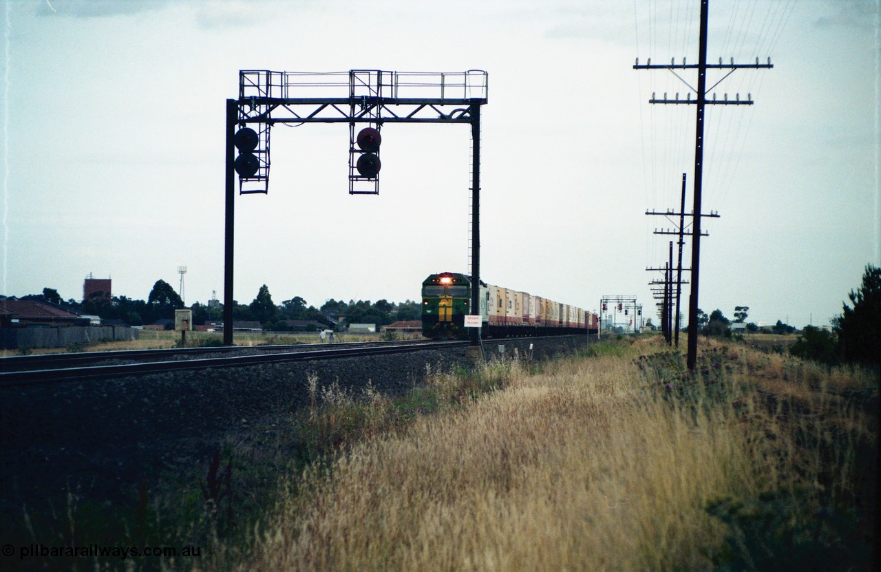 159-01
Deer Park West, broad gauge Australian National BL class locomotive leads an Adelaide bound down goods train near Robinson Road, signal gantry for up movements with searchlight signals 1/22 and 1/10, the sign on the signal gantry is for 'UNSAFE DECKING'.
