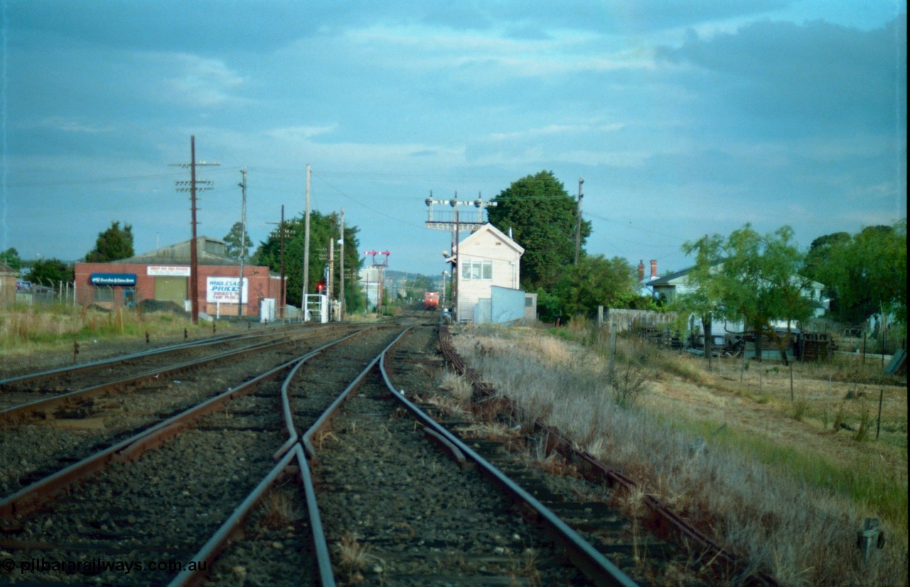 159-17
Ballarat D Signal Box, Linton Junction, broad gauge track view from the Cattle Yard Line looking east, Linton Line then the Ararat Line with the down crossover visible, triple doll semaphore signal 20 facing down train is visible behind the signal box, with the Gillies Street interlocked gates open, staff exchange platform and up home semaphore signal post 19, down home semaphore signal post 18 is visible and pulled off to allow the approaching train to pull up to Gillies Street, points, track work and point rodding.
