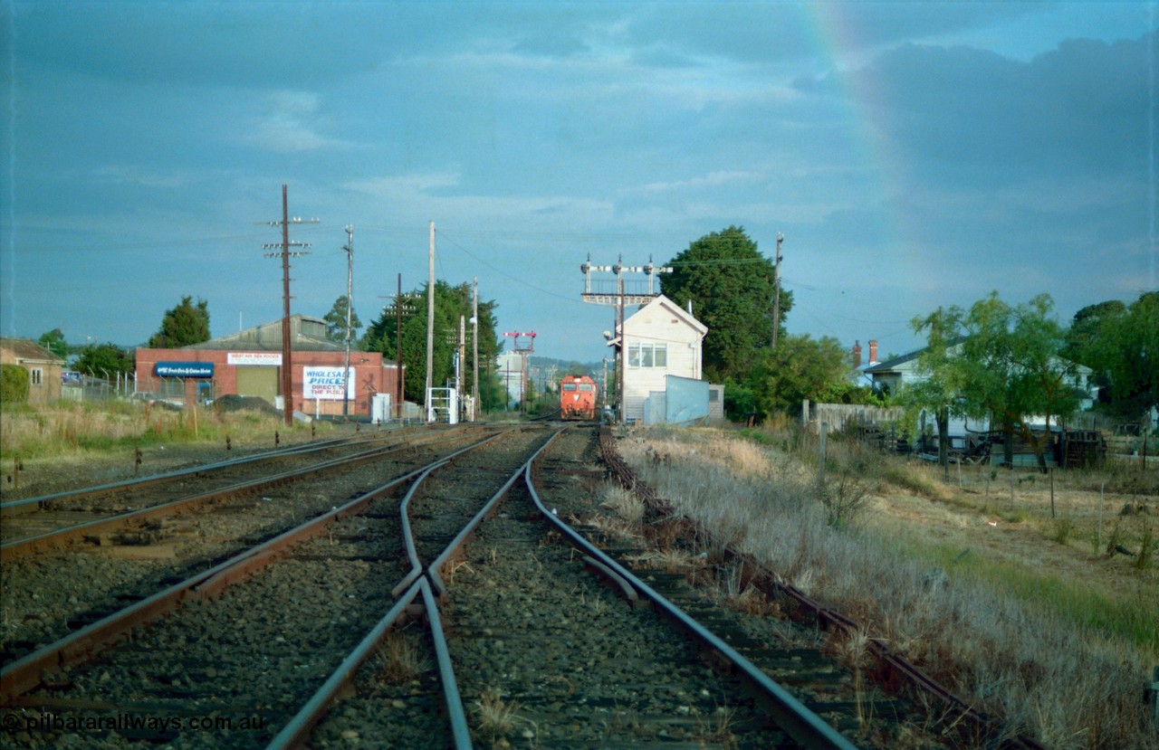 159-18
Ballarat D Signal Box, Linton Junction, broad gauge track view from the Cattle Yard Line looking east, Linton Line then the Ararat Line with the down crossover visible, triple doll semaphore signal 20 facing down train is visible behind the signal box, with the Gillies Street interlocked gates open, staff exchange platform and up home semaphore signal post 19, down home semaphore signal post 18 is visible and now back at stop as the approaching train with a V/Line G class comes to a stand just east of Gillies Street, points, track work and point rodding.
