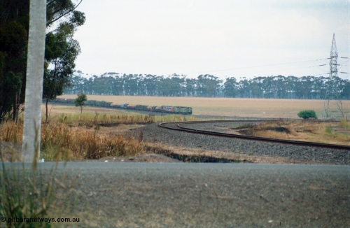 159-12
Lismore, distant view across Gnarpurt Road grade crossing of Australian National broad gauge BL class BL 27 Clyde Engineering EMD model JT26C-2SS serial 83-1011 leading a sister BL class and V/Line S and X class locomotives with down goods train 9169 as it runs round the curves on their way to Adelaide.
