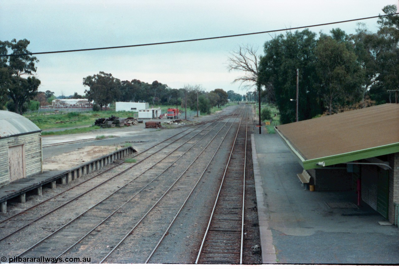 161-01
Numurkah, station yard overview looking south towards Melbourne from footbridge, brick station building and platform, curved roof goods shed and platform at left, redundant semaphore signal post 3 visible beyond platform, track gang work compound.
