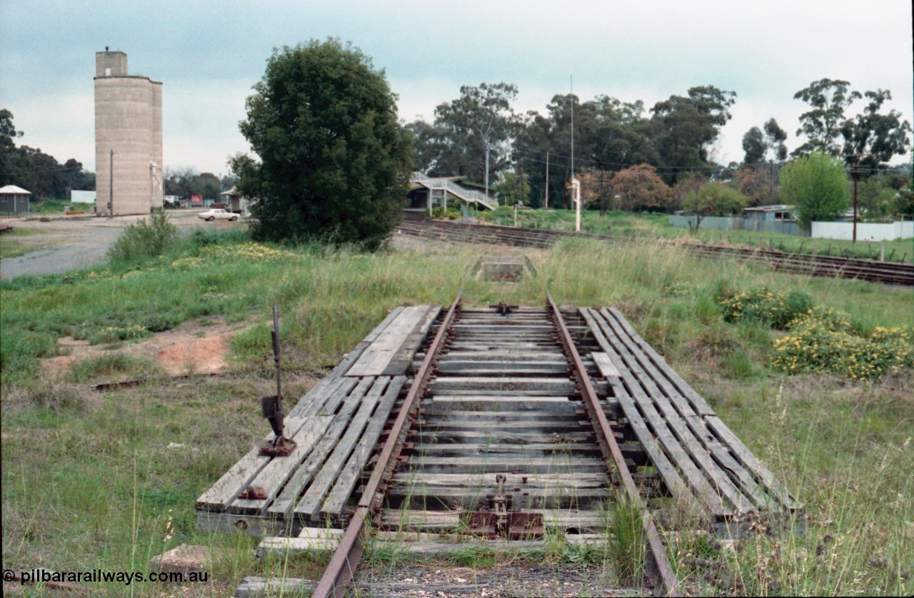 161-07
Numurkah, yard view looking south from turntable track, open deck and pit with locking lever, ash pit visible along with steam era water stand pipe on No.1 Rd, Williamstown style silo complex on the left with goods shed obscured by tree, HK Holden sedan, station building and steel lattice footbridge in the middle of frame.
