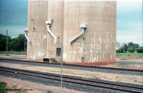 161-11
Katunga, view across tracks from former station site, location sign missing from post, station name painted on Williamstown style silo complex, three train loading spouts.
