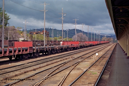 166-0A
Albury South station yard view looking south from platform, V/Line broad gauge loaded Up Albury slab steel train 9334 waits for some locos and departure time later in the day, NSWSRA slab steel waggons and trans-shipping gantry crane on the left. The V/Line broad gauge platform is just visible on the right.
