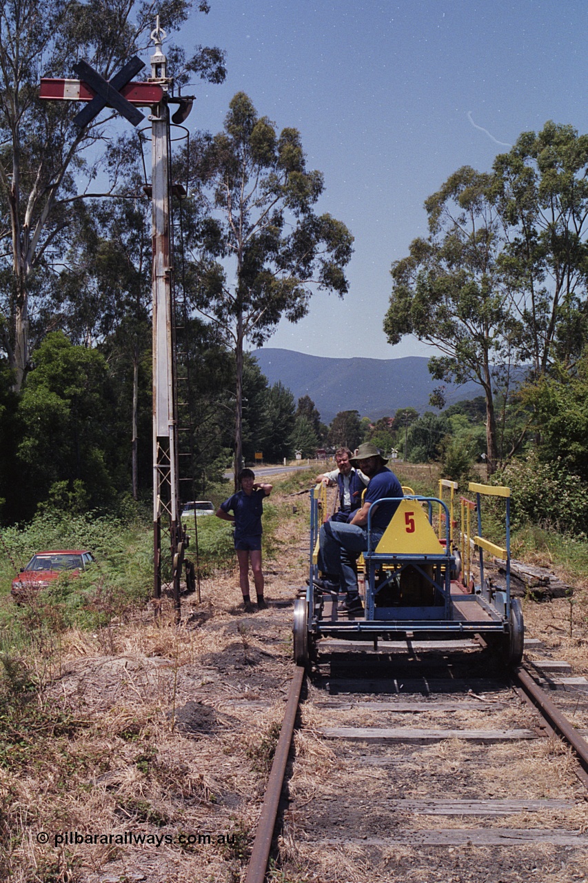 168-19
Healesville, broad gauge ganger's trolley #5 at the down home semaphore signal post with some YVTR volunteers, black cross on semaphore means signal not in use.
