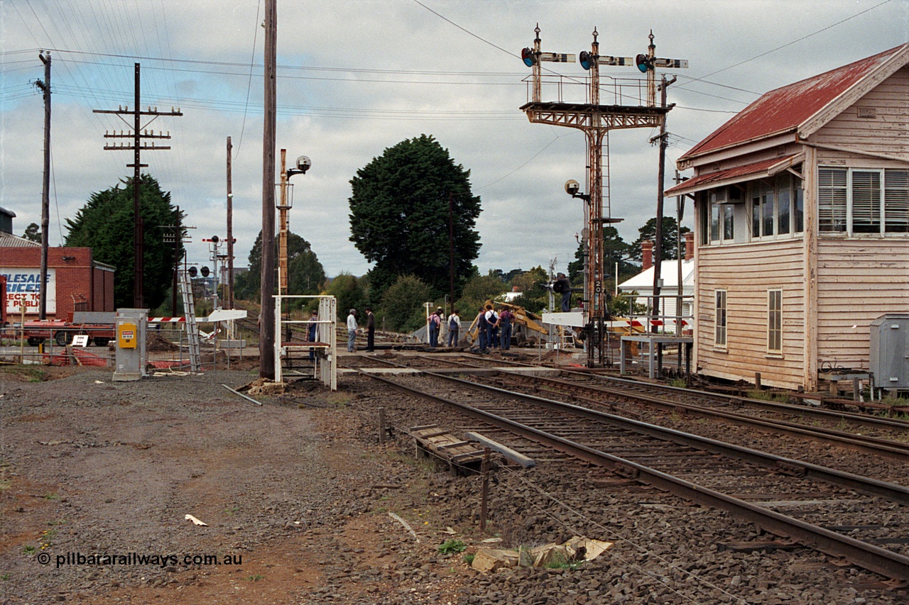 171-03
Ballarat, Linton Junction signal box Gillies St, work site view, interlocked gates being replaced by boom barriers, view of signal box, triple doll semaphore signal Post 20, Timken's Siding disc signal Post 21, staff exchange platform and auto exchange apparatus cover open, track view.
