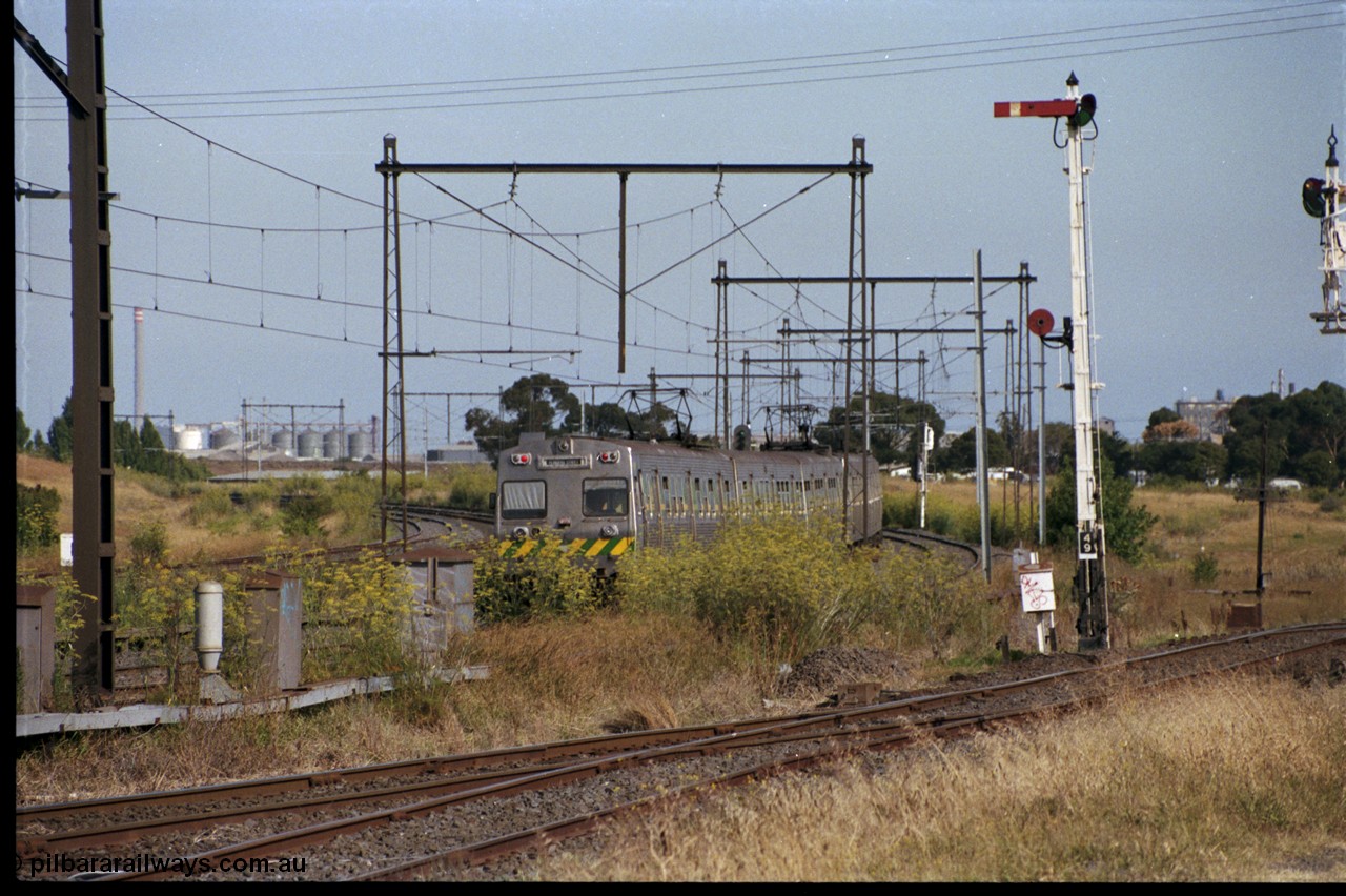 172-01
Sunshine, broad gauge Melbourne metropolitan electric service operated by 'The Met', this up Hitachi 6 car 'spark' or electric train rounds the curve east of Sunshine as it heads to Tottenham, signal post 49 controls up trains on the Sunshine - Newport Loop Line, with the disc controlling access to the GEB sidings, the points facing the camera leads to the main running lines and the Sunshine yard or what remained of it.
