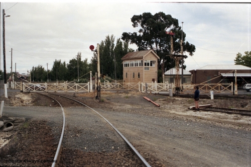 172-36
Ballarat East signal box, track view looking across interlocked swing gates at Humffray St, looking west towards Ballarat, signal box framed between semaphore signal post 5 and disc signal post 6. Disc signal 6 is down home from Loco Tracks to Post 15 controlled by A Box, Post 5 left doll is Down Home No. 2 to Post 11 via Passenger Line controlled by A Box.
