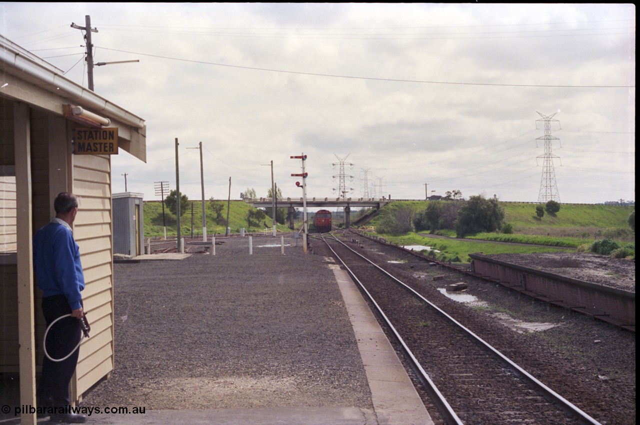 179-09
Gheringhap, station yard view looking west from the station building as the signaller stand by with an electric staff in a hoop as he prepares to swap staves with down loaded grain train 9122 coming off the Ballarat line behind a pair of V/Line G class locomotives led by G 515 Clyde Engineering EMD model JT26C-2SS serial 85-1243, the Midland Highway overpass frames the train with signal post 4. The former up platform is visible on the right and the pit where the removed double mainline used to be is clearly visible.
Keywords: G-class;G515;Clyde-Engineering-Rosewater-SA;EMD;JT26C-2SS;85-1243;