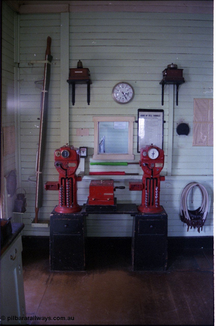 179-32
Gheringhap, internal view of signal box showing the electric staff instruments for the North Geelong C section on the left and the Meredith section on the right, above each exchanger is the respective bell for each section, along with wall clock and Code of Bell Signals wall chart, to left is a station stretcher and hand lamp and on the right the electric staff carriers or hoops. At the very left of frame the train register desk can be just seen, through the opening in the wall behind the exchangers can be seen the 18+2 lever frame levers.
