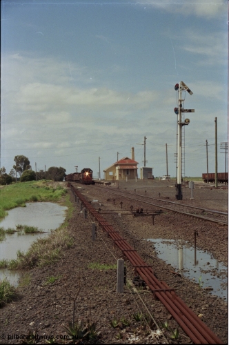 179-04
Gheringhap, yard overview looking east, broad gauge V/Line down goods train 9153 departs for Maroona with the signal on post 4 pulled off for the Maroona line, point rodding and interlocking is spaced away from the line as this location used to have double mainlines, on the right are gypsum waggons in Sidings B.
Keywords: X-class;X53;Clyde-Engineering-Rosewater-SA;EMD;G26C;75-800;