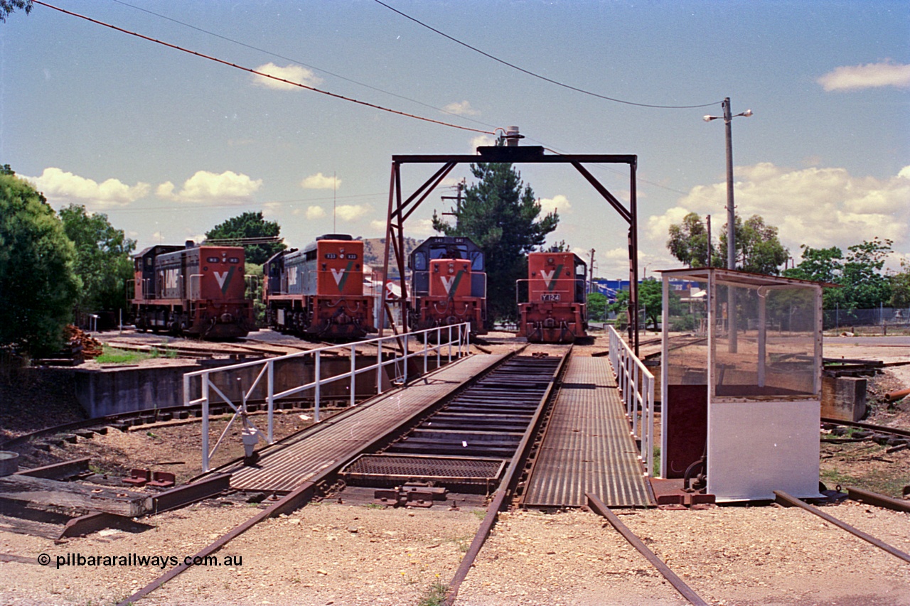 180-28
Wodonga loco depot, turntable area finds a variety of V/Line broad gauge motive power in the form of H class H 3 Clyde Engineering EMD model G18B serial 68-631, X class units X 33 Clyde Engineering EMD model G16C serial 66-486 and X 41 Clyde Engineering EMD model G26C serial 70-704 and Y class shunt loco Y 124 Clyde Engineering EMD model G6B serial 63-314, the electric turntable control cabin and interlocking lever and stub roads are clearly visible.
