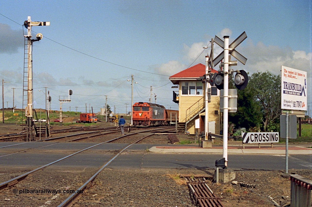 185-04
North Geelong C Box looking across the Separation Street grade crossing as a V/Line G class locomotive departs North Geelong Yard with 9121 empty grain train, the signaller has the Gheringhap electric staff ready to hand up to the driver, the tracks to the grain loop and the Loop Line to Melbourne are curving around to the left beyond the mechanical and electric signal posts.
Keywords: G-class;G514;Clyde-Engineering-Rosewater-SA;EMD;JT26C-2SS;85-1242;