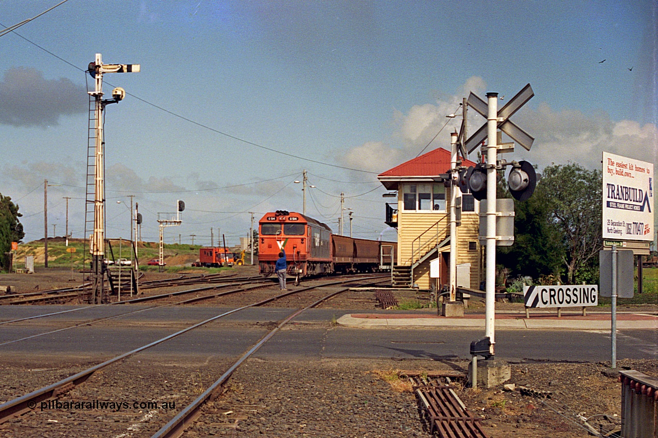 185-05
North Geelong C Box looking across the Separation Street grade crossing as a V/Line G class locomotive G 514 Clyde Engineering EMD model JT26C-2SS serial 85-1242 departs North Geelong Yard with 9121 empty grain train, the signaller has the Gheringhap electric staff offered up to the driver, the tracks to the grain loop and the Loop Line to Melbourne are curving around to the left beyond the mechanical and electric signal posts.
Keywords: G-class;G514;Clyde-Engineering-Rosewater-SA;EMD;JT26C-2SS;85-1242;