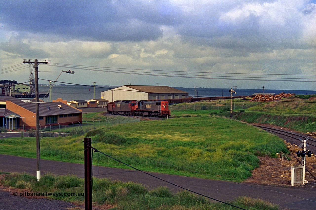 185-09
North Geelong Grain Loop view from Corio Quay Road across to Corio Quay with Access Road and grade crossing, and the former tracks to South Quay visible at the left corner, the grain train is approaching the Home Signal that protected the former Freezing Works Siding.
