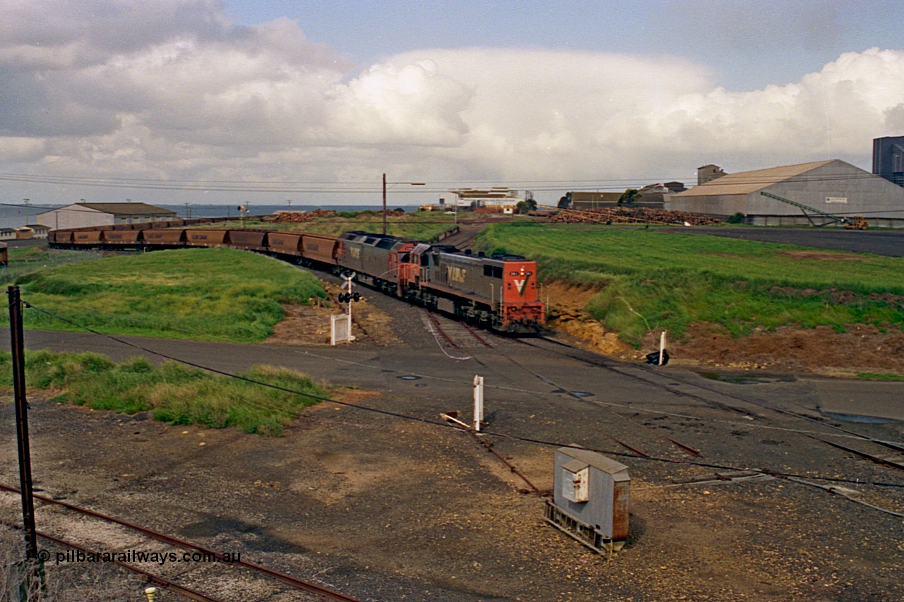 185-11
North Geelong Grain Loop view from Corio Quay Road across Access Road grade crossing with the tracks to Corio Quay at the very bottom of image, as the grain train behind V/Line locos X class locomotive X 41 Clyde Engineering EMD model G26C serial 70-704 long end leading and G class locomotive G 528 Clyde Engineering EMD model JT26C-2SS serial 88-1258 having past the Home Signal and crossing the former tracks for the Freezing Works Sidings.
Keywords: X-class;X41;Clyde-Engineering-Granville-NSW;EMD;G26C;70-704;