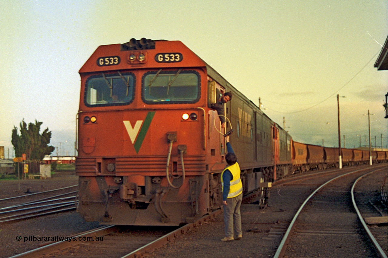 185-34
North Geelong C Box, V/Line down grain train number 9125 departs the yard as the driver leans out the window and collects the electric staff off the signaller for the section to Gheringhap from the cab of G class G 533 Clyde Engineering EMD model JT26C-2SS serial 88-1263, with a sister unit trailing, ground dwarf disc signal post 18 is pulled off for the move.
Keywords: G-class;G533;Clyde-Engineering-Somerton-Victoria;EMD;JT26C-2SS;88-1263;