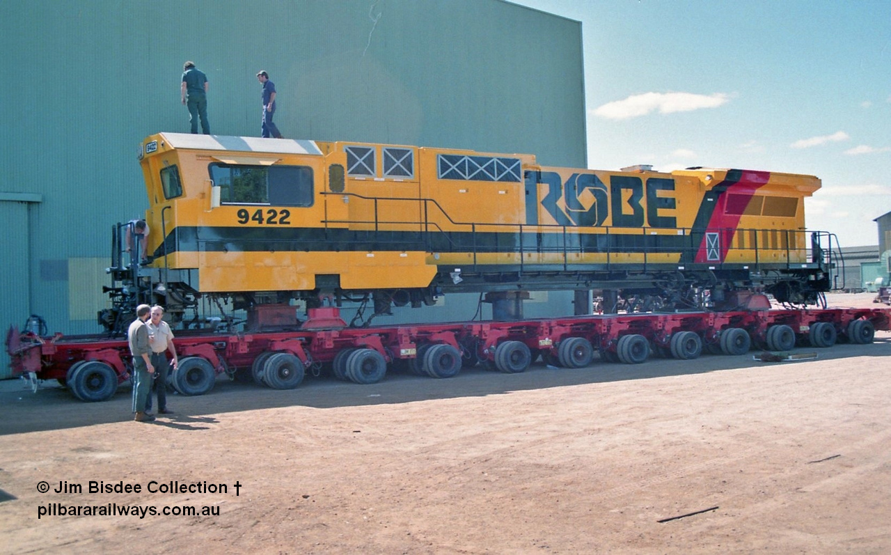 23100
Bassendean, Goninan workshops, loaded onto a hundred and four six wheel road transport float, Robe River rebuild GE CM40-8M unit 9422 serial 8297-03 / 93-138 is loaded awaiting transport to Cape Lambert. 9422 was rebuilt from Comeng NSW built ALCo M636 9422 serial C6103-2 from Aug 1977 and kept this number when rebuilt here. March 1993.
Jim Bisdee photo.
Keywords: 9422;Goninan;GE;CM40-8M;8297-03/93-138;rebuild;Comeng-NSW;ALCo;M636;C6103-2;