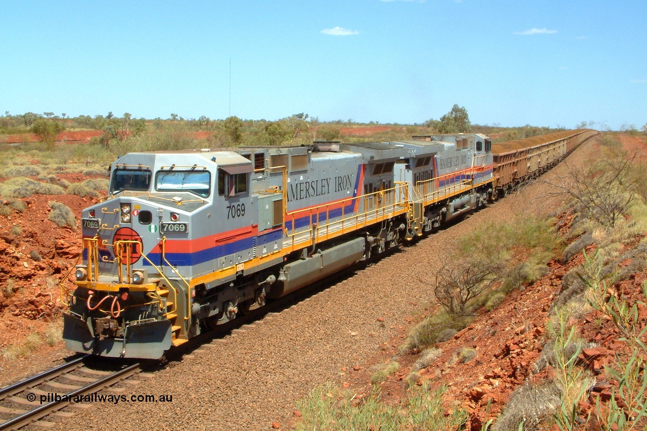 050110 140552r
Having departed Ibis Siding five minutes earlier double General Electric built Dash 9-44CW Hamersley Iron units 7069 serial 47748 and 7077 serial 47756 work a 230 loaded waggon train heading north between Ibis and Gull sidings. Above the two locos the east mainline can be seen in the background which was part of the second last duplication project from Gull to Tunkawanna and is a single track section with only passing tracks being on the original west mainline section. Monday 10th January 2005.
Keywords: 7069;GE;Dash-9-44CW;47748;